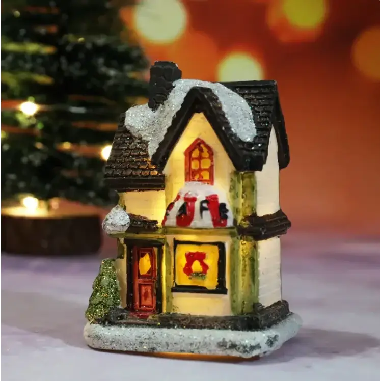 A miniature christmas house with a black roof, white walls, and glowing windows featuring red holiday decorations.
