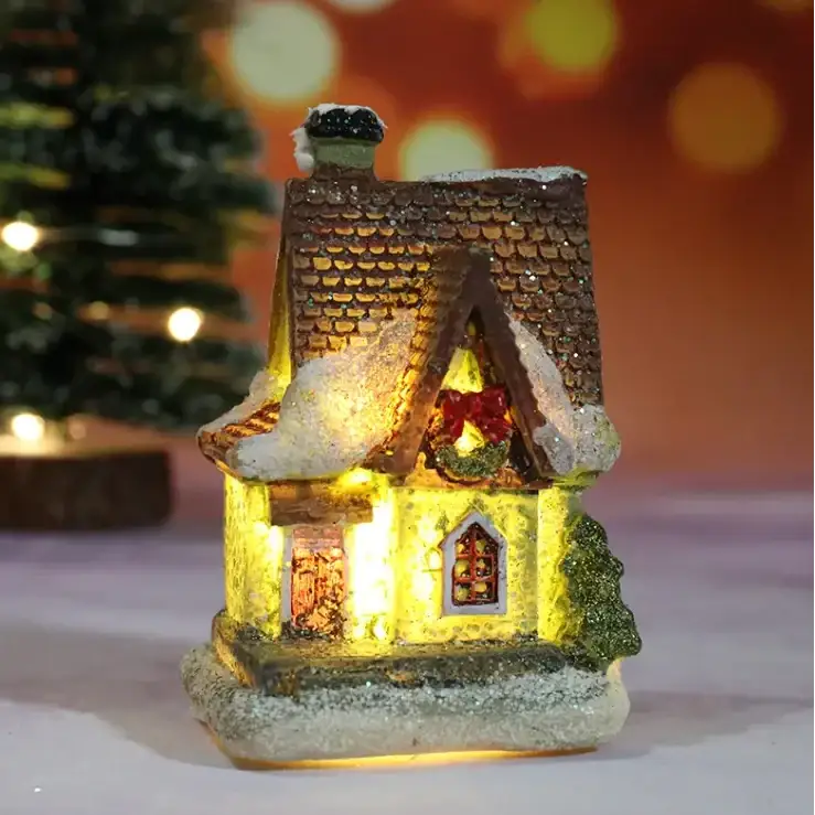 A miniature illuminated christmas house with a brown shingled roof, snow-dusted details, and warm yellow interior lighting.