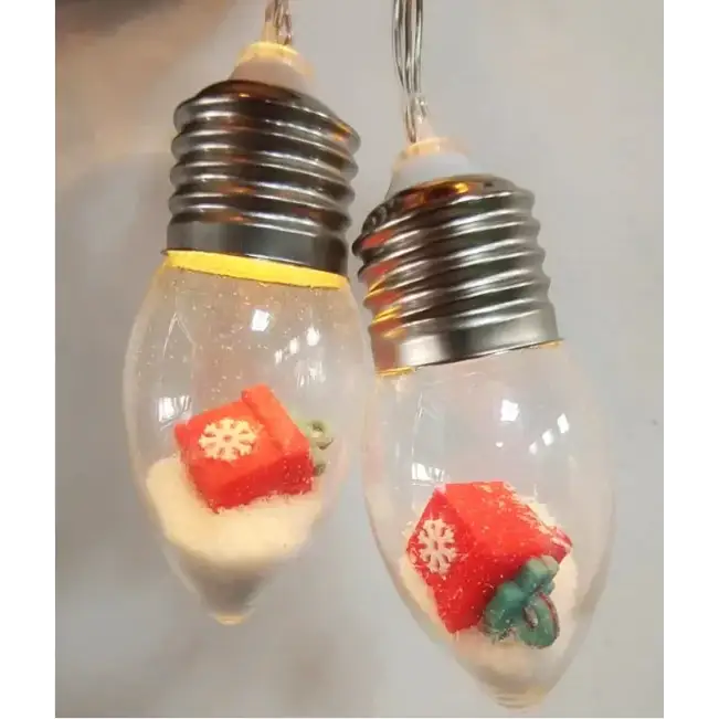 Clear glass light bulb ornaments with metallic screw bases, each containing a red gift box figurine and white glittery sand.
