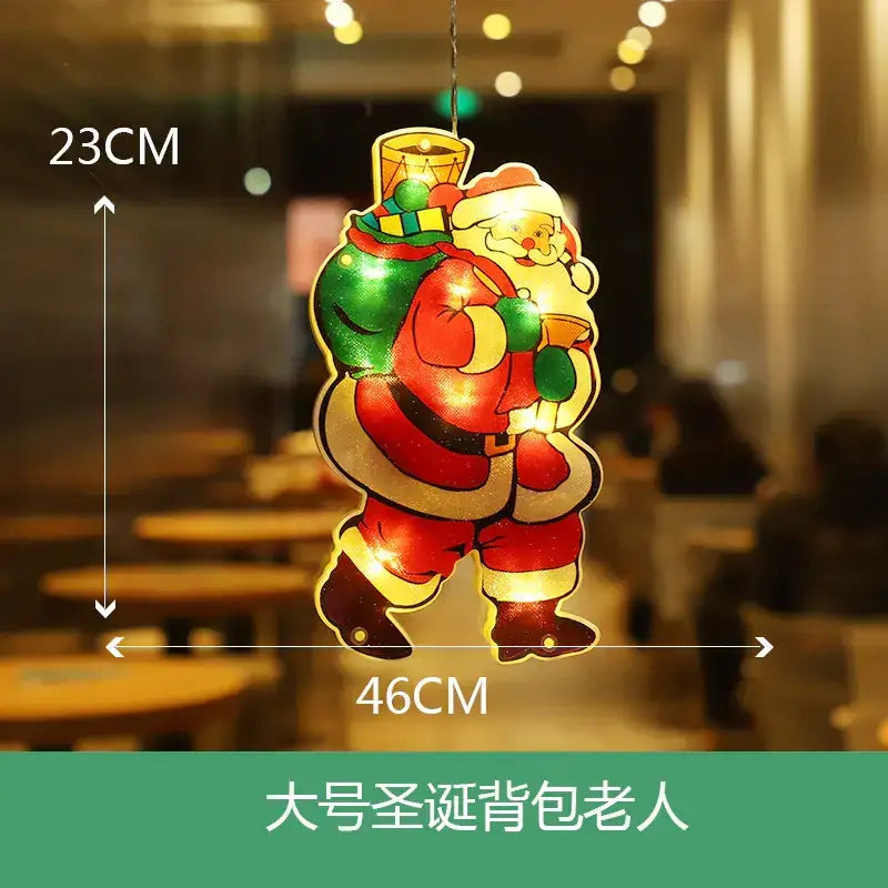 A glowing, 23cm by 46cm illuminated santa claus hanging ornament with a red suit and green sack.