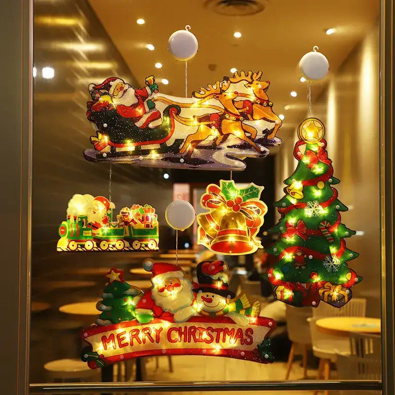 Christmas-themed illuminated window decals featuring santa in a sleigh, reindeer, a train, bells, and trees with glowing lights.
