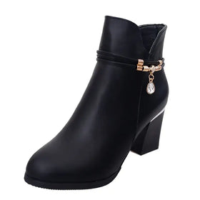 Black faux leather ankle boot with a chunky heel and a decorative gold-toned buckle featuring a dangling crystal teardrop charm.