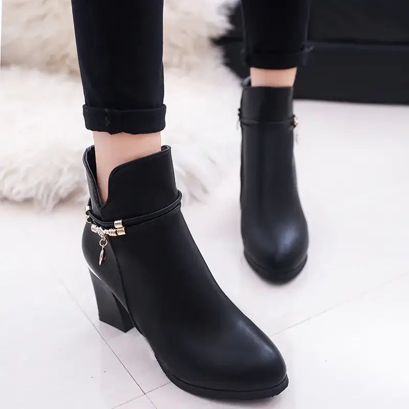 Black leather ankle boot with a chunky heel and decorative gold-tone chain detail at the side.