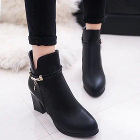 Black leather ankle boot with a chunky heel and decorative gold-tone chain detail at the side.