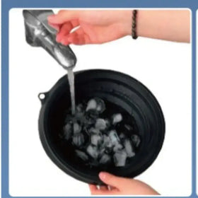 Black collapsible bowl filled with ice cubes being rinsed under running water from a faucet.