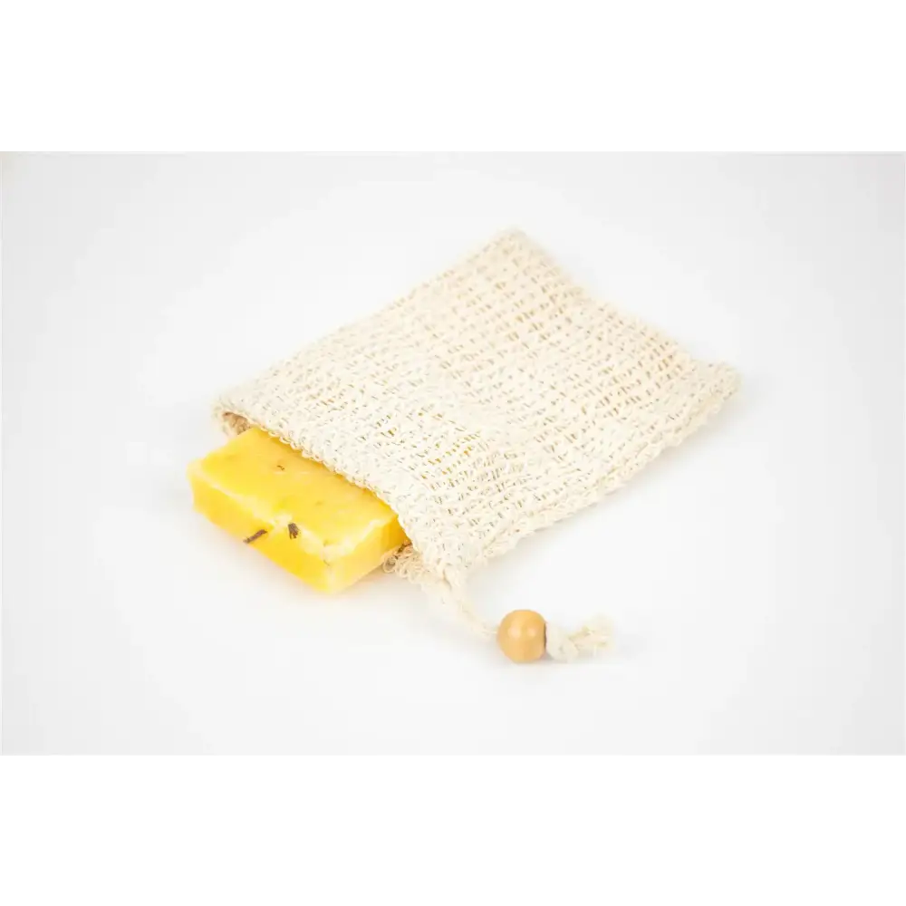A beige, knitted mesh soap bag with a wooden toggle closure holds a rectangular yellow bar of soap.