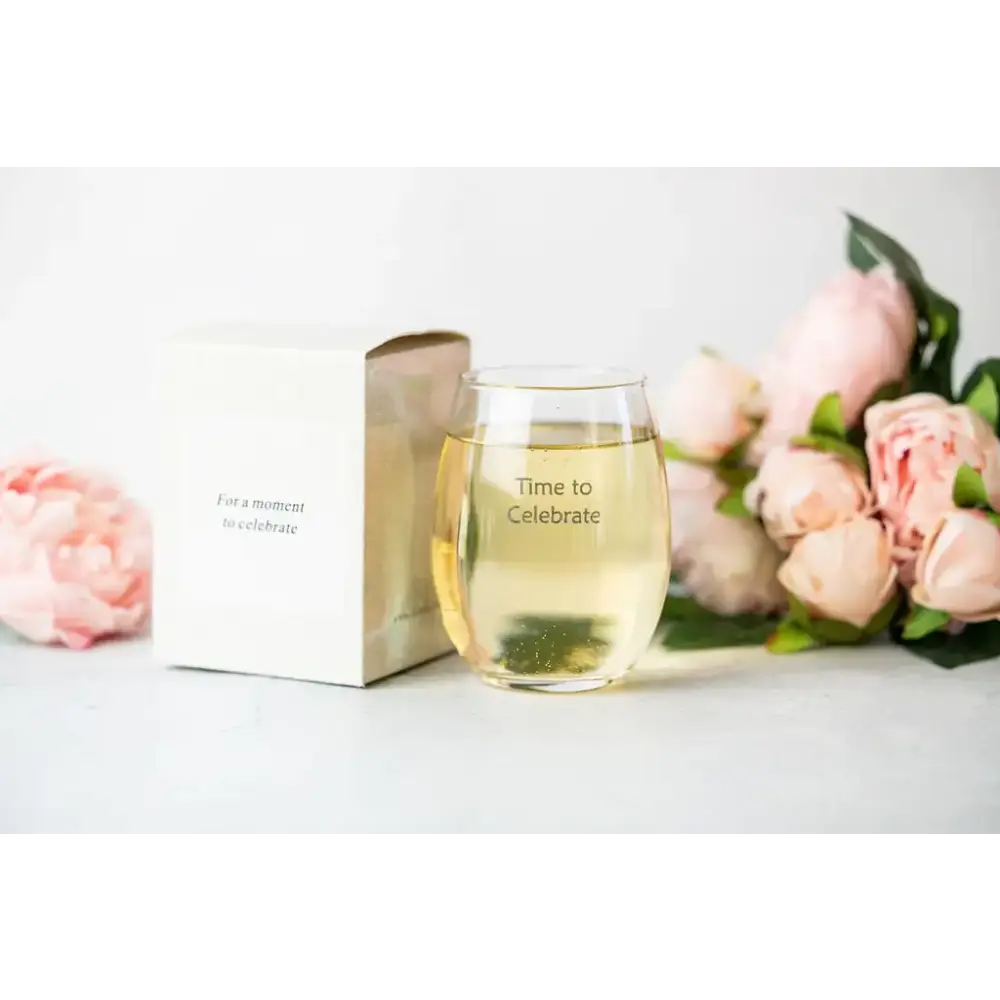 Clear stemless wine glass with ’time to celebrate’ engraved in a simple sans-serif font, filled with golden-hued liquid.