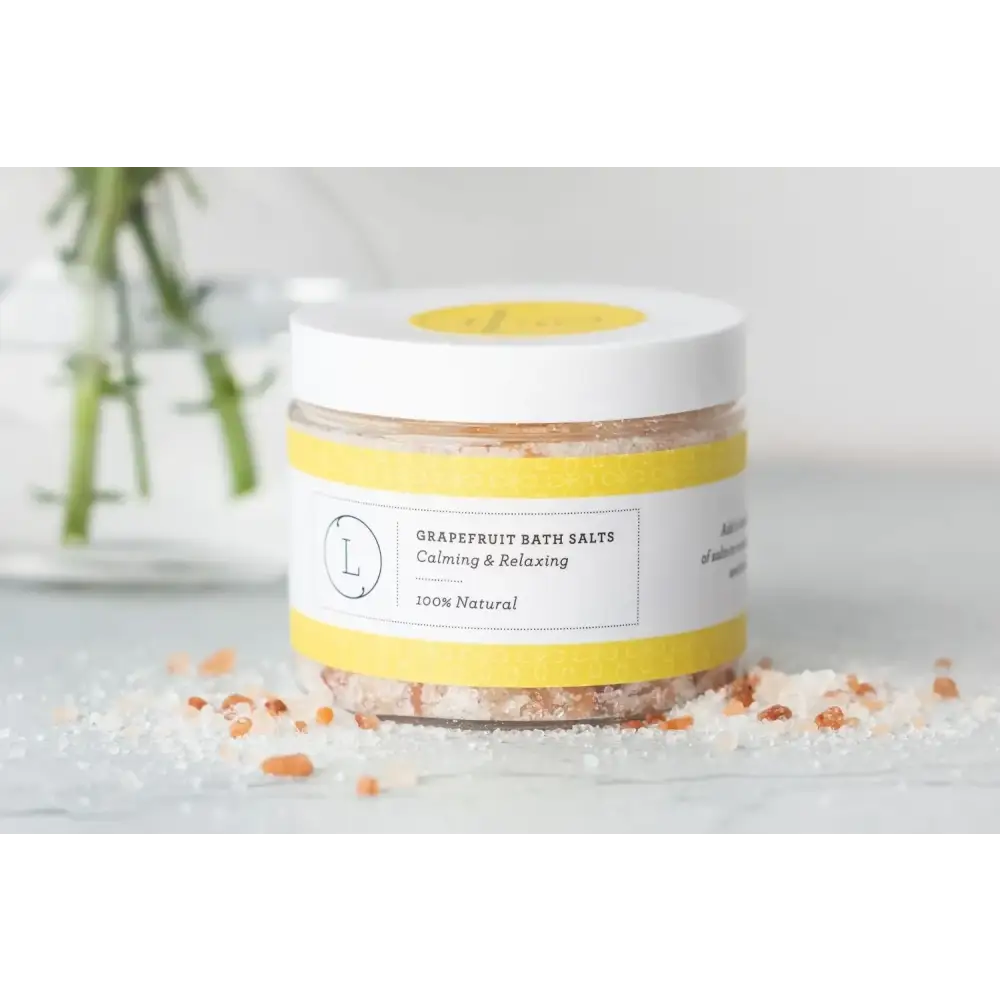 A jar of grapefruit bath salts with a white lid and yellow label, containing pinkish-orange crystalline salt.