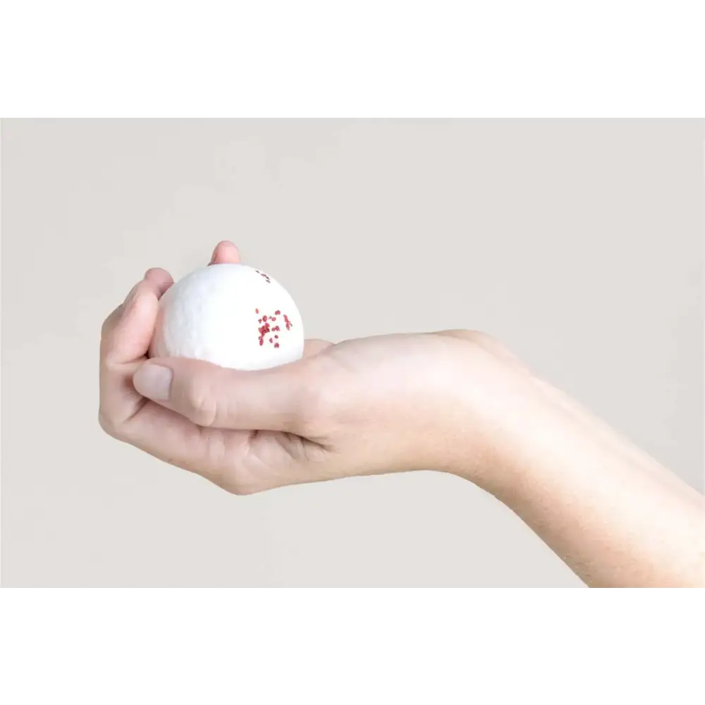 A white golf ball with small red speckles on its surface, held gently in a person’s hand.