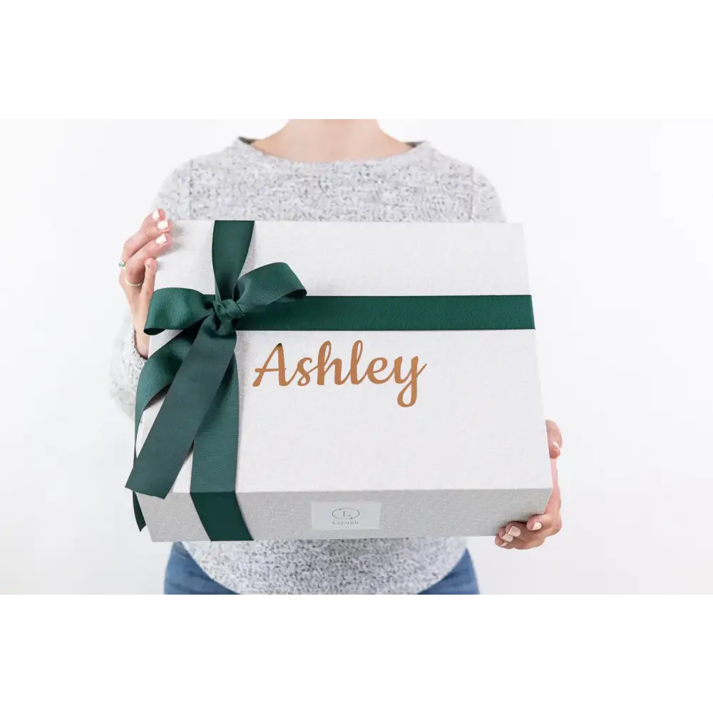 White gift box with a dark green ribbon bow and the name ’ashley’ in gold cursive lettering.