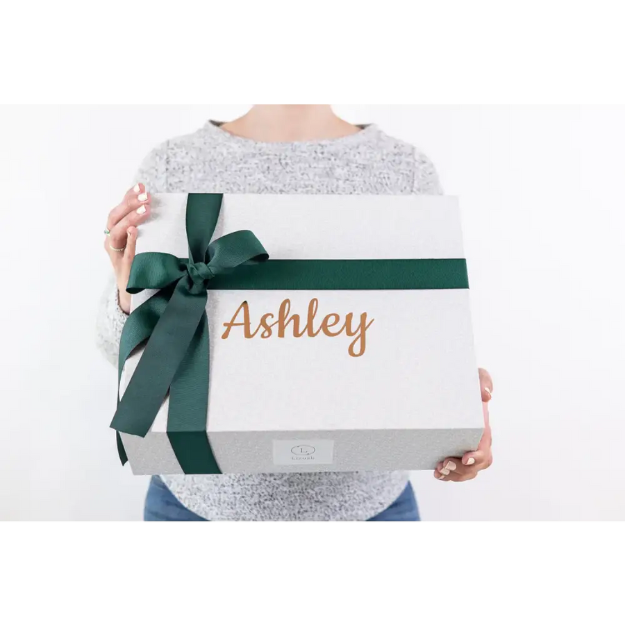White gift box with a dark green ribbon bow and the name ’ashley’ in gold cursive lettering.