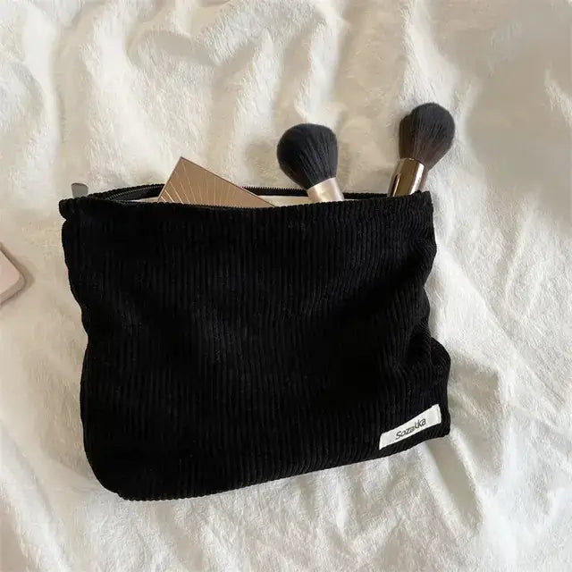 Black corduroy makeup pouch with a white label.