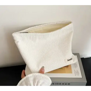 A cream-colored corduroy clutch with a subtle textured weave and a small embroidered brand tag on the corner.