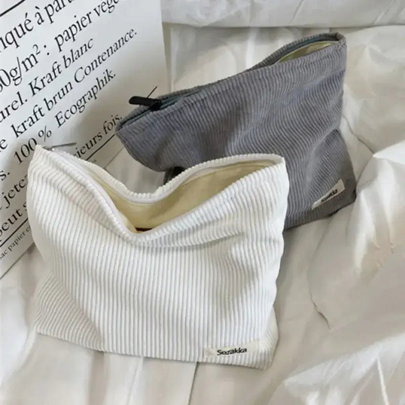 White corduroy pouch with a zipper closure and a small brand label on the corner.