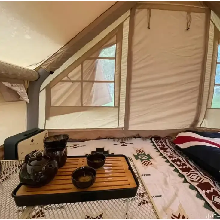 Dark ceramic tea set with a glossy finish, arranged on a wooden tray inside a tent.