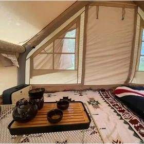 Dark ceramic tea set with a glossy finish, arranged on a wooden tray inside a tent.