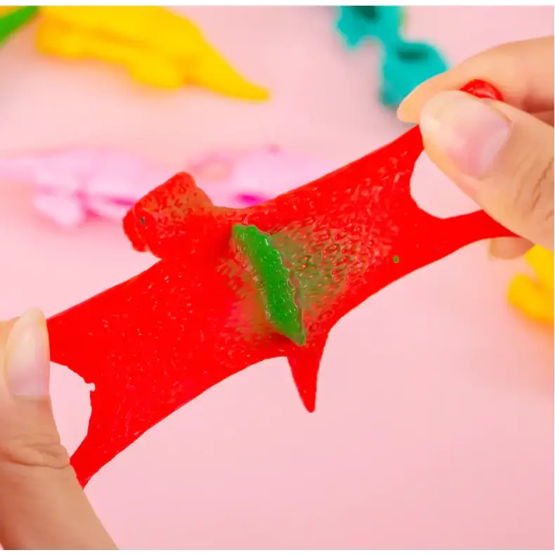 A vibrant red, translucent gummy dinosaur with a green gummy piece embedded in its body.