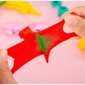 A vibrant red, translucent gummy dinosaur with a green gummy piece embedded in its body.