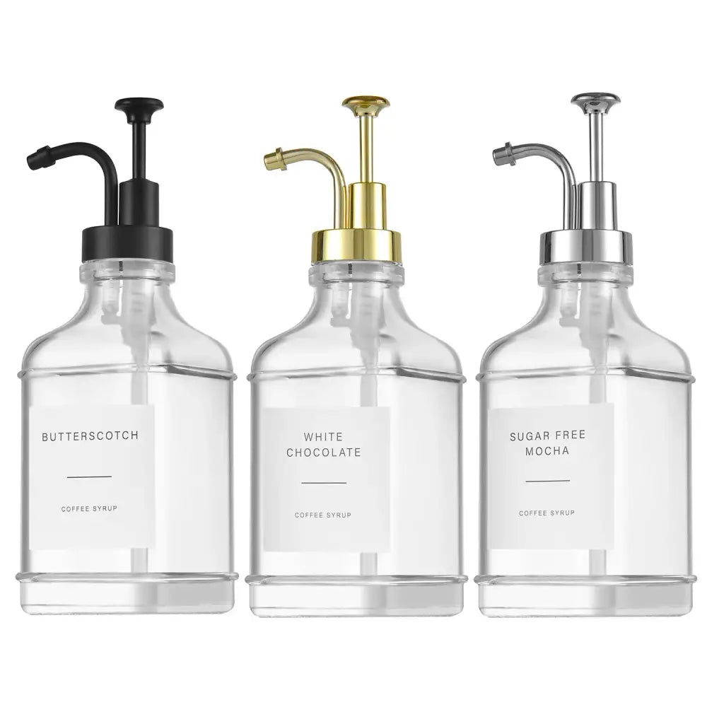 Three clear glass syrup dispensers with black, gold, and silver pump tops.