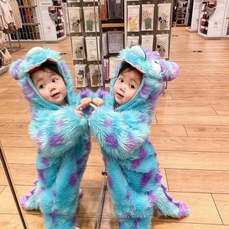 Two toddlers in matching fluffy blue and purple monster costumes with long tails, hooded heads featuring large white eyes.