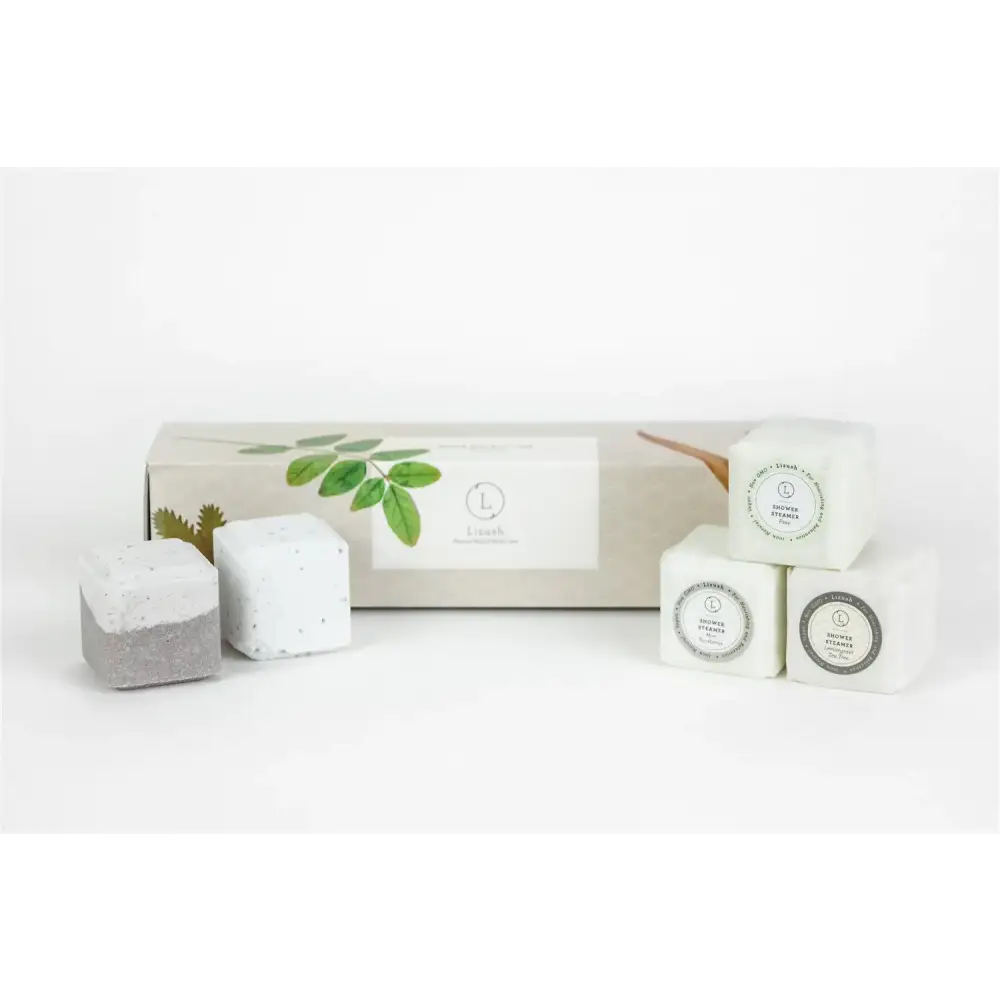 White and gray bath bombs with a speckled texture, packaged in an elegant box adorned with green leaf motifs.