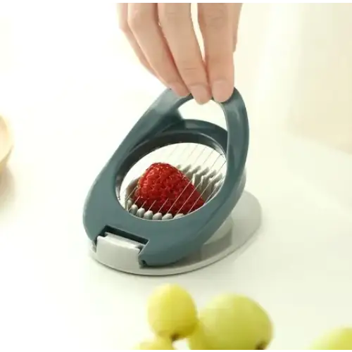 A sleek, dark gray handheld strawberry slicer with a circular metal grid and white plastic accents.