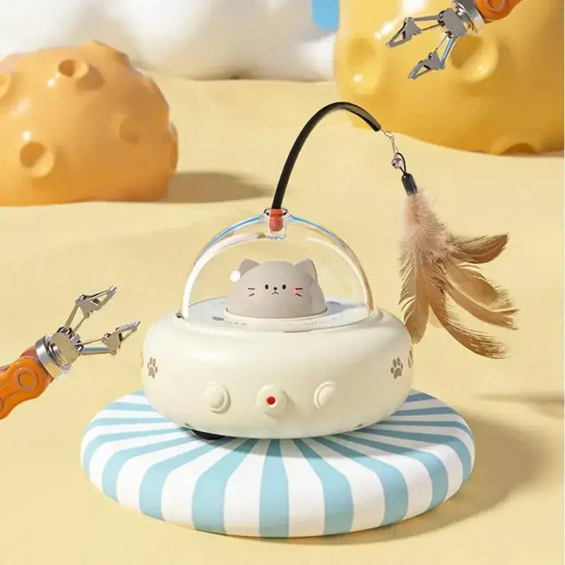 A cute gray cat-shaped toy in a transparent dome sits atop an off-white, paw-print decorated base with three buttons and a red indicator light.