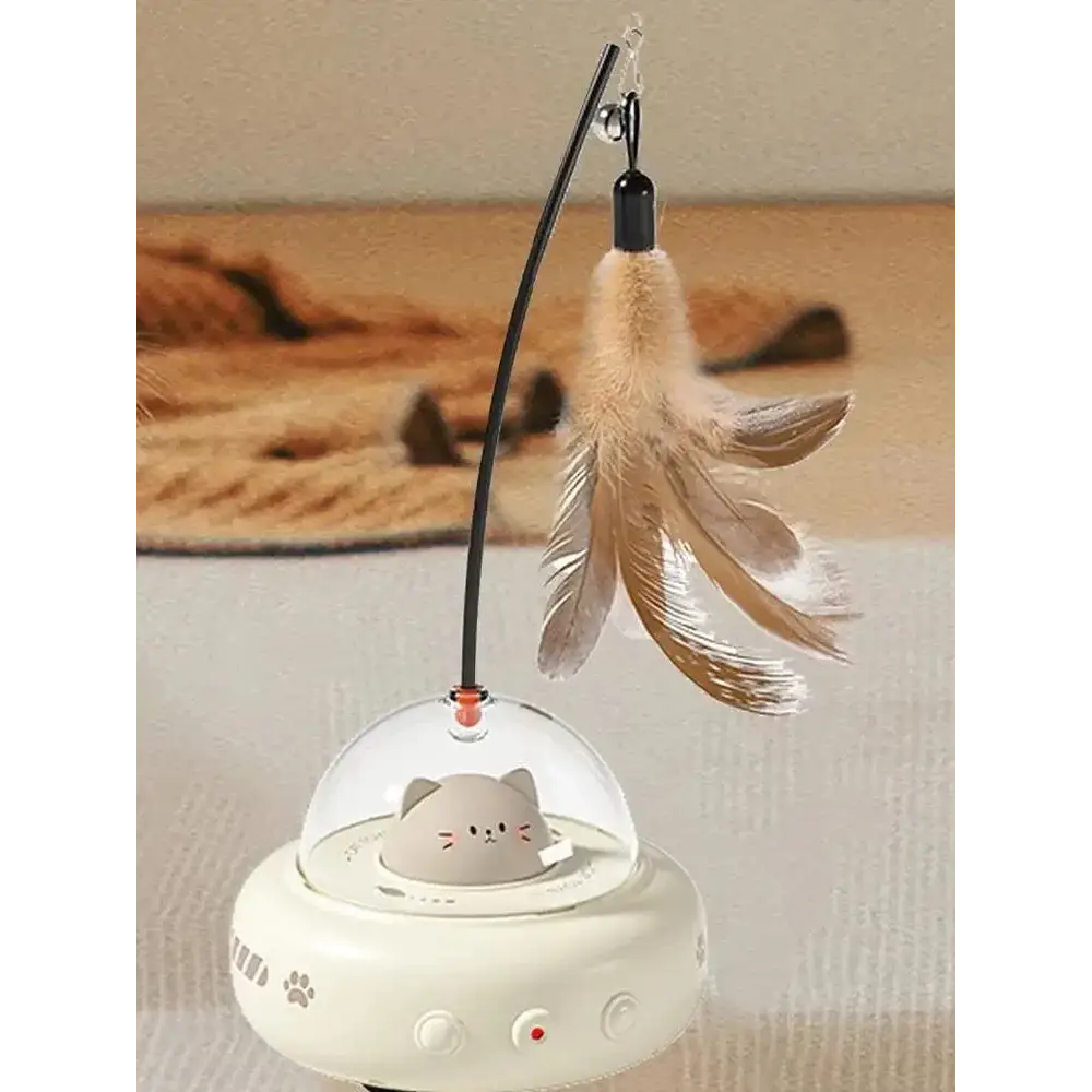 A white, ufo-shaped cat toy with a clear dome housing a gray cartoon cat figure and featuring paw print decals on its base.