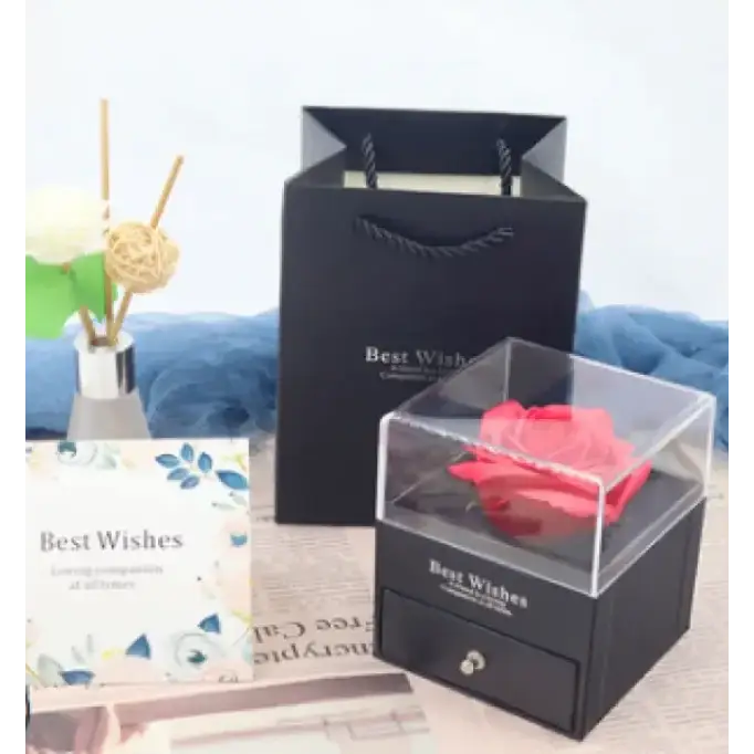 A vibrant red preserved rose nestled inside a clear acrylic display box with a black base and drawer.