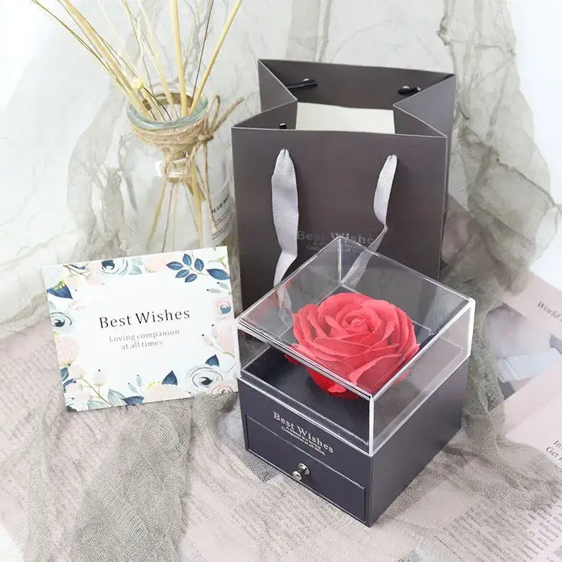 A vibrant pink preserved rose nestled inside a clear acrylic box with a black drawer base, elegantly presented as a gift.