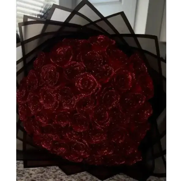 A lush bouquet of deep red, glittery roses arranged in a black geometric paper wrap.