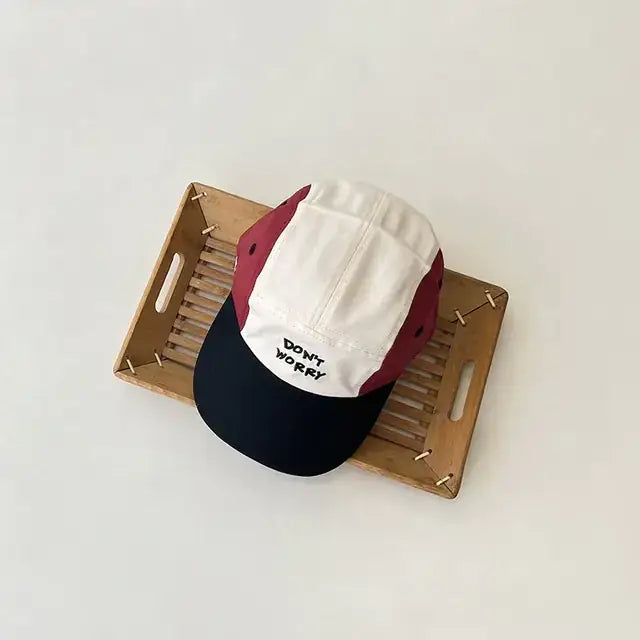 A maroon, white, and navy blue five-panel baseball cap with ’don’t worry’ embroidered in black on the front.
