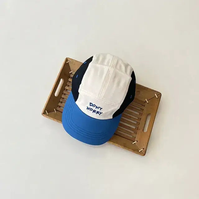 A blue, white, and black baseball cap with ’don’t worry’ embroidered in navy on the front.