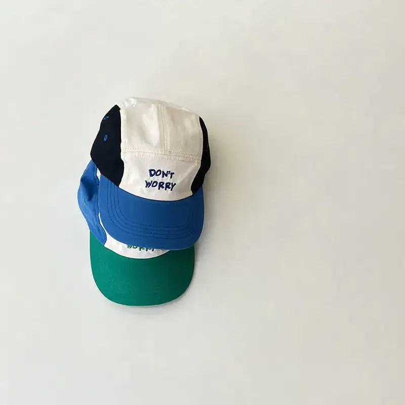 A colorful, multi-panel baseball cap with a white front panel featuring the embroidered text ’don’t worry’ in blue thread.