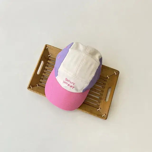 Pastel-colored baseball cap with a white front panel, lavender side panels, and a pink brim, featuring the embroidered phrase ’don’t worry’ in red thread.