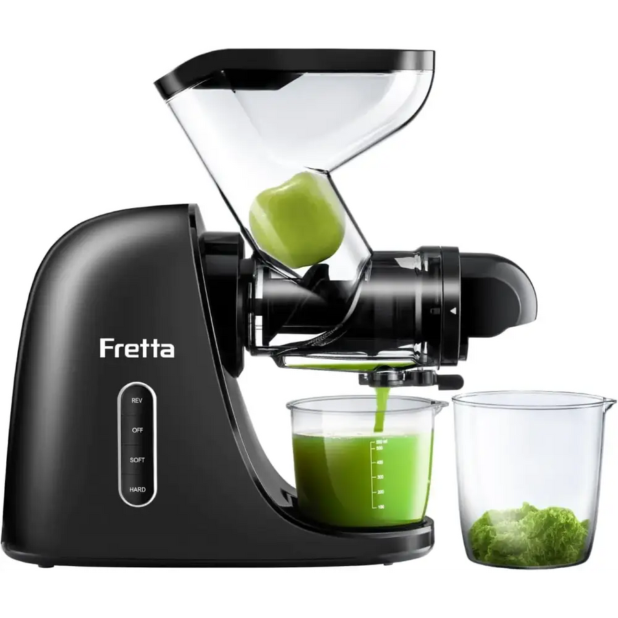 Black fretta juicer with transparent feed chute and clear collection cups, actively extracting green juice from a fruit.