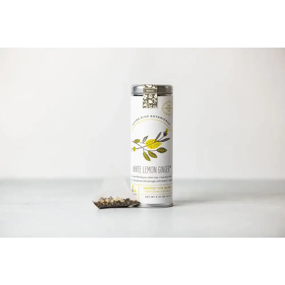 A sleek white cylindrical tin with a silver lid and botanical illustrations, labeled ’white lemon ginger’ by living bird botanica.