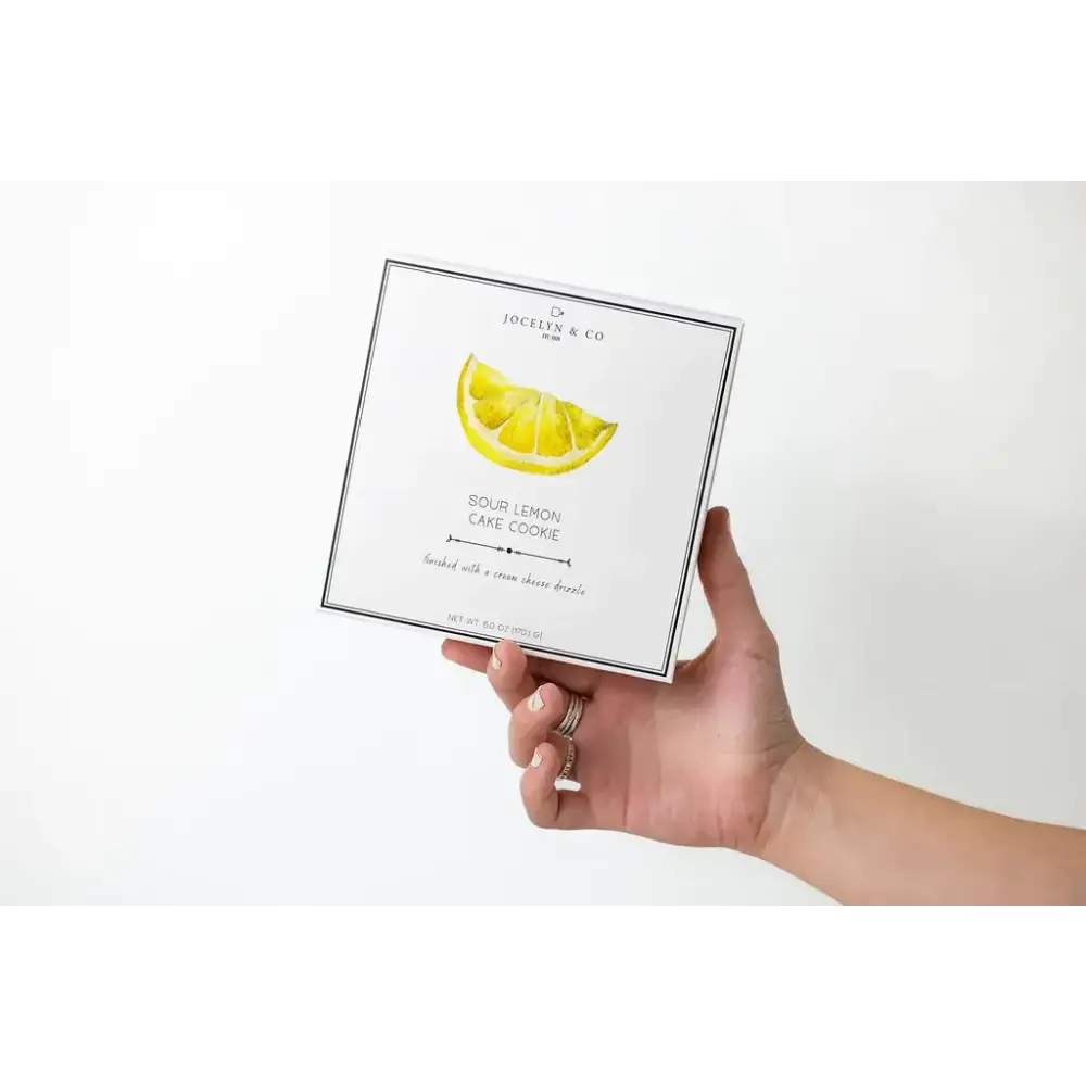 A white rectangular box with a black border, featuring an illustration of a lemon slice and the text ’sour lemon cake cookie’ by jocelyn & co.