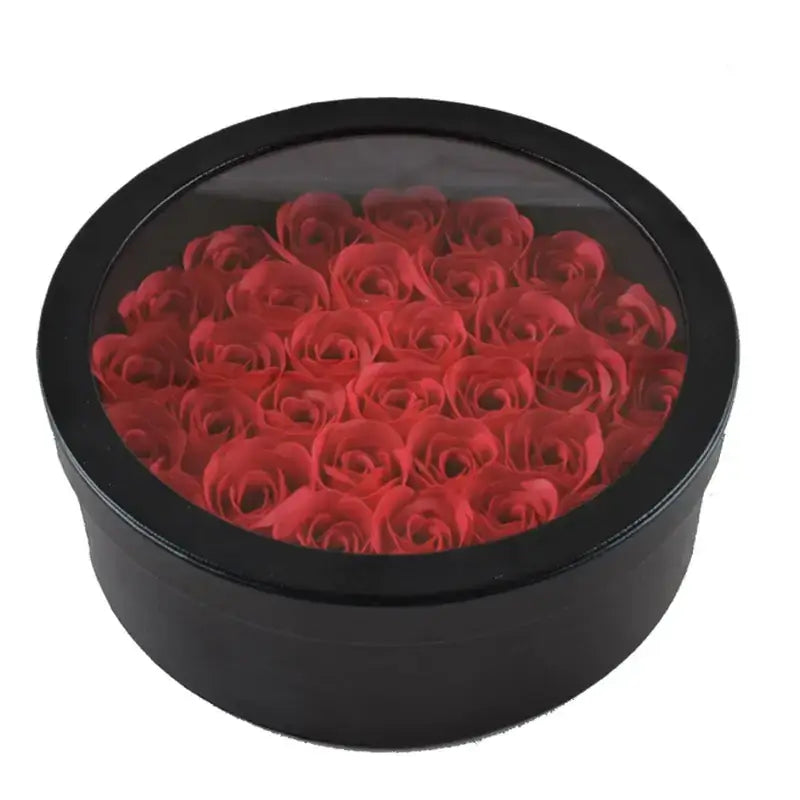 Black circular box with a clear lid, filled with vibrant red artificial roses.