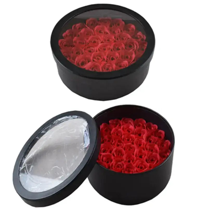 Black circular gift box with a clear lid, filled with vibrant red artificial roses.