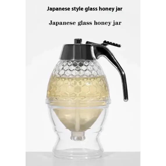 Clear glass honey jar with a black metal spout and handle, featuring an intricate hexagonal pattern on its body.