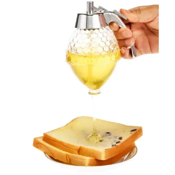 A clear glass honey dispenser with a silver metal pump and handle, featuring a textured hexagonal pattern on its body.