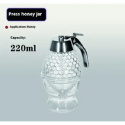 Clear glass honey press jar with a silver-toned metal handle and lid, featuring an intricate hexagonal pattern on its body.