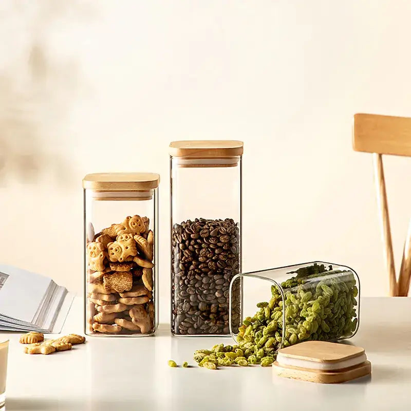 Clear glass storage jars with bamboo lids, filled with assorted dry goods like cookies and coffee beans.