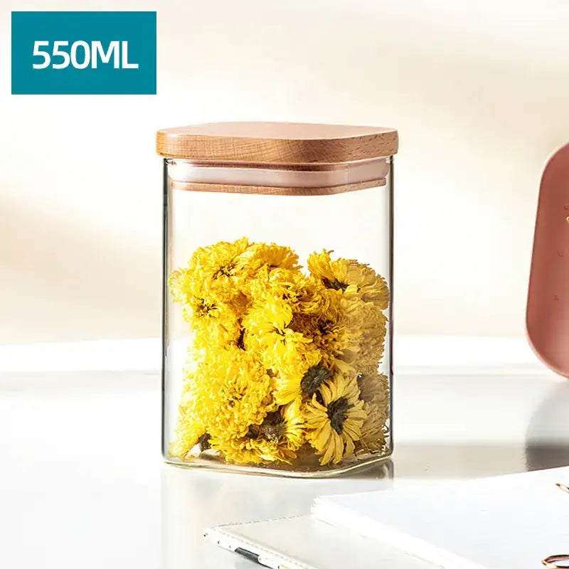 Clear glass storage jar with a square wooden lid, filled with vibrant yellow dried flowers.