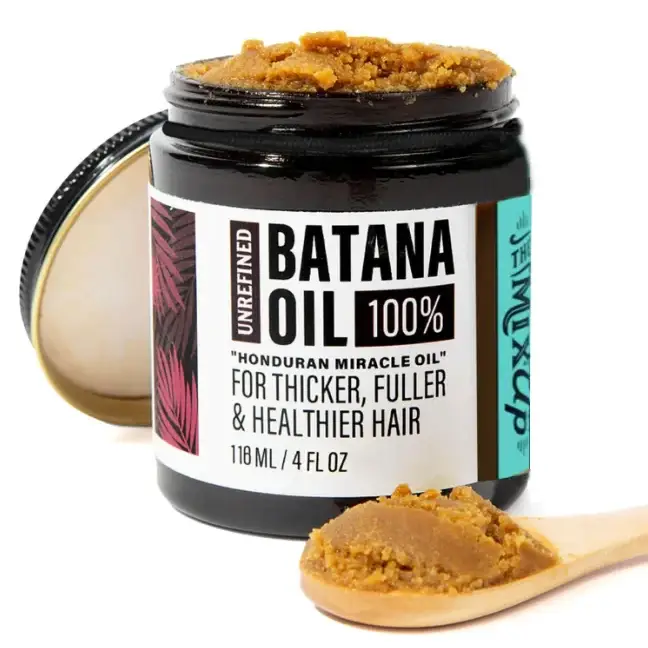 A jar of unrefined batana oil, a dark amber-colored, textured hair treatment in a black glass container with a white and teal label.