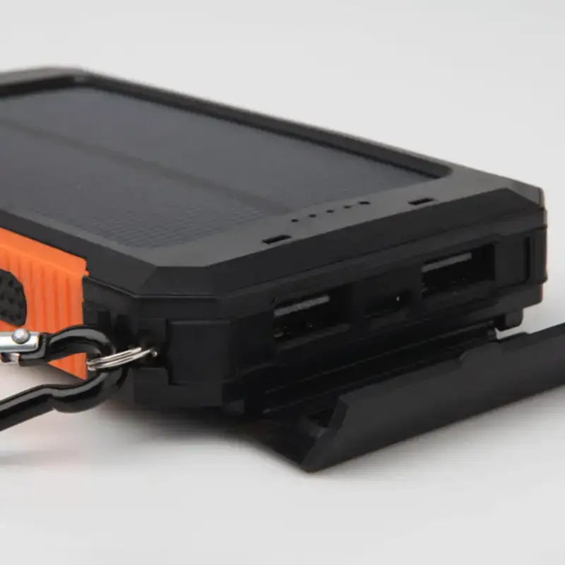 Black and orange rugged solar-powered portable charger with usb ports and a keychain attachment.