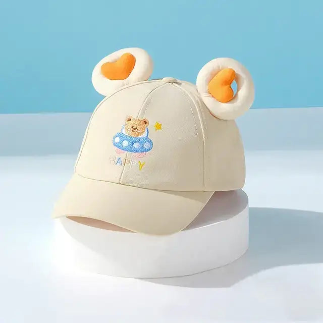 Beige baseball cap with plush bear ears and embroidered teddy bear in a ufo, featuring ’happy’ text.