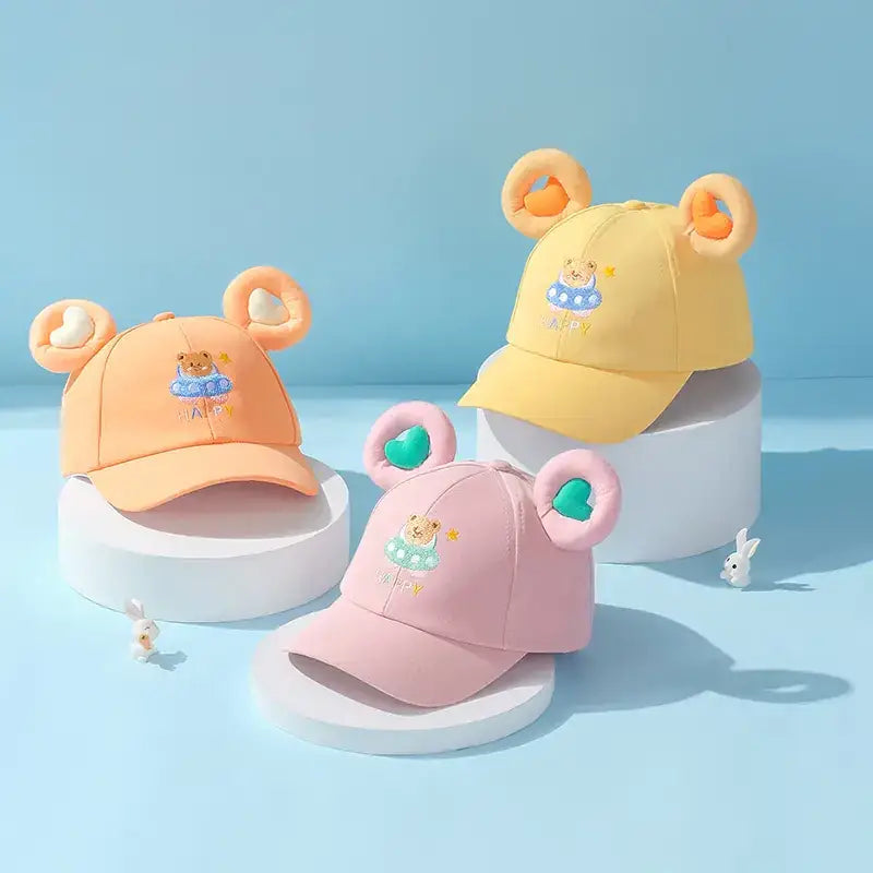Pastel-colored toddler baseball caps with plush bear ears and embroidered teddy bears in swimwear