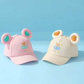Pink and cream-colored toddler baseball caps featuring plush bear ears with heart-shaped cutouts, each adorned with an embroidered teddy bear in a swimsuit.